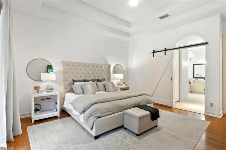Bedroom featuring a barn door, baseboards, visible vents, a raised ceiling, and wood finished floors