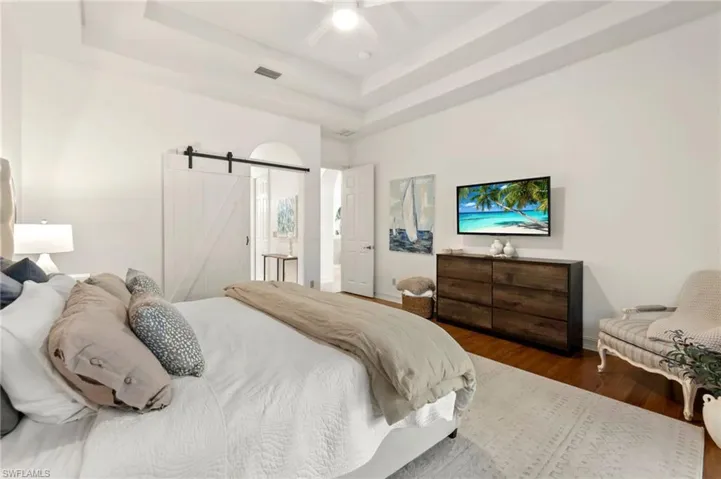 Bedroom with a barn door, wood finished floors, visible vents, a ceiling fan, and a tray ceiling