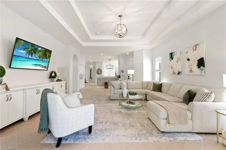 Living room featuring a chandelier, a tray ceiling, arched walkways, and light tile patterned floors