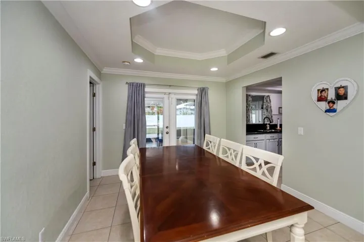 Dining room featuring french doors, ornamental molding, light tile floors, and a raised ceiling