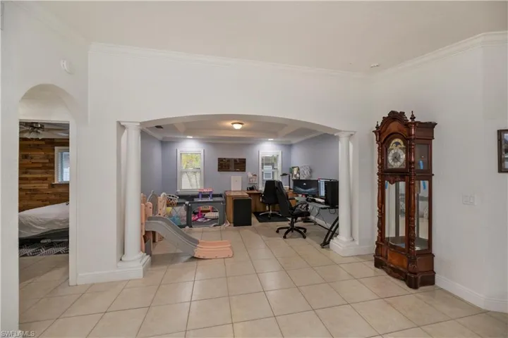 Office space featuring crown molding, ceiling fan, ornate columns, and a raised ceiling