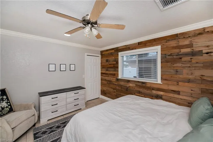 Tiled bedroom with wooden walls, a closet, ceiling fan, and crown molding