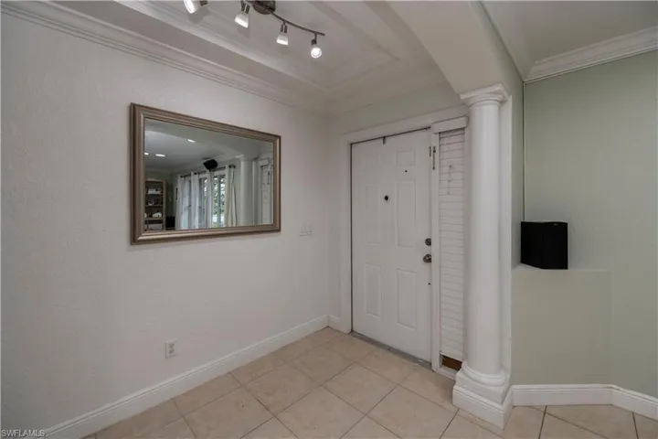 Tiled entryway featuring crown molding, track lighting, and decorative columns