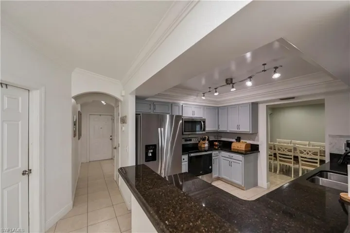Kitchen with ornamental molding, stainless steel appliances, a tray ceiling, rail lighting, and sink
