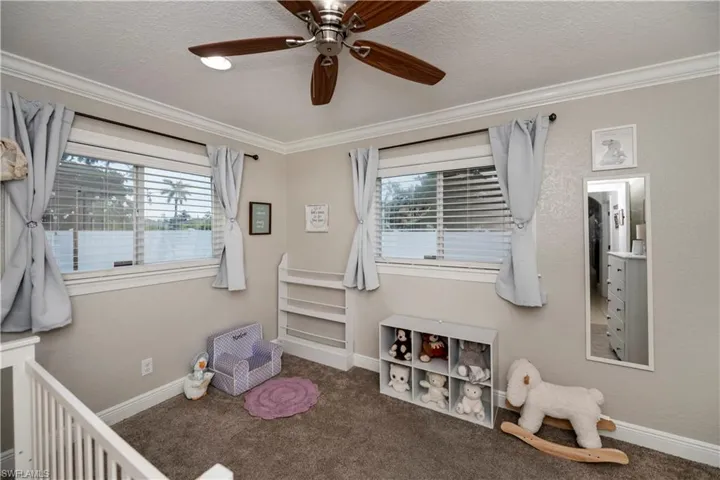Bedroom featuring ceiling fan, crown molding, a textured ceiling, dark colored carpet, and a nursery area