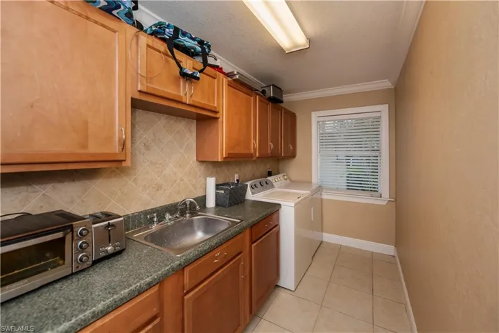 Clothes washing area featuring light tile flooring, separate washer and dryer, crown molding, sink, and a textured ceiling