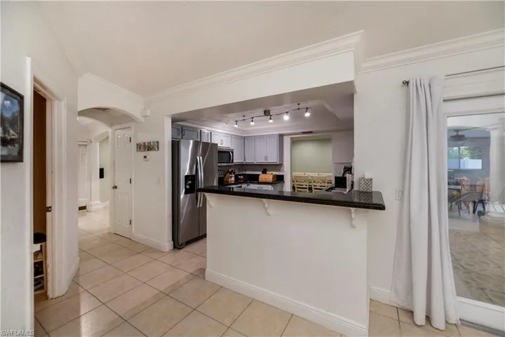 Kitchen with ornamental molding, stainless steel appliances, kitchen peninsula, rail lighting, and light tile floors