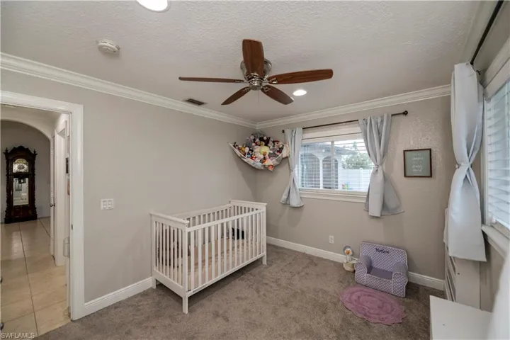 Carpeted bedroom featuring crown molding, a textured ceiling, a crib, and ceiling fan