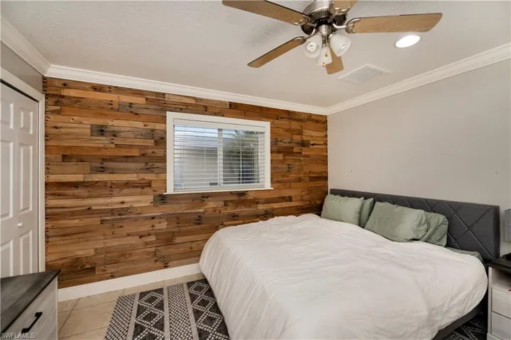 Tiled bedroom featuring wooden walls, a closet, ceiling fan, and crown molding