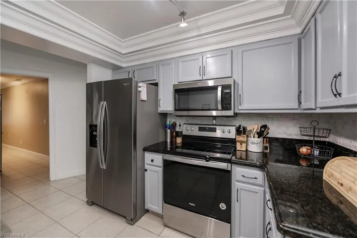 Kitchen featuring appliances with stainless steel finishes, a tray ceiling, ornamental molding, and dark stone countertops