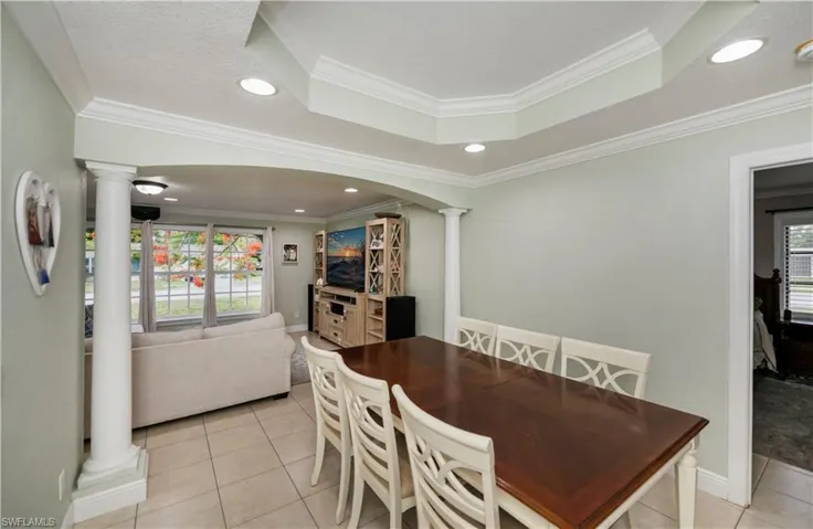 Tiled dining room featuring a raised ceiling, ornamental molding, and ornate columns