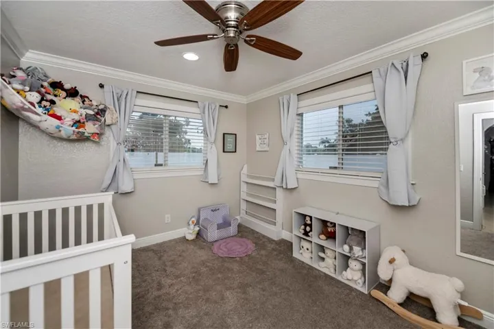 Carpeted bedroom with multiple windows, crown molding, a crib, and ceiling fan