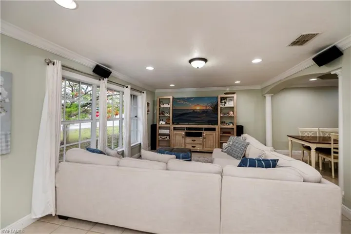 Living room with crown molding, ornate columns, and light tile floors
