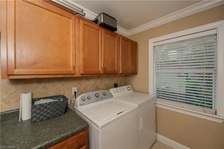 Laundry area featuring washing machine and dryer, ornamental molding, and cabinets