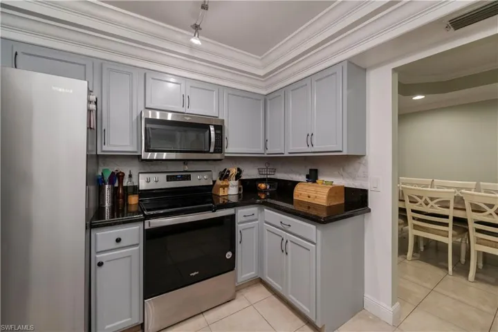 Kitchen featuring stainless steel appliances, ornamental molding, light tile flooring, and backsplash
