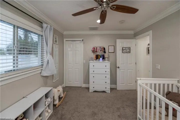 Carpeted bedroom featuring a nursery area, a closet, ceiling fan, and ornamental molding