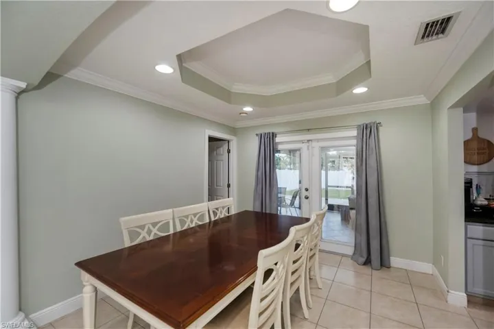 Dining space featuring ornamental molding, a tray ceiling, light tile flooring, and french doors