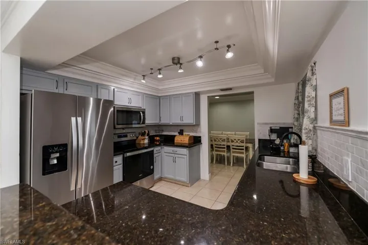 Kitchen featuring appliances with stainless steel finishes, a tray ceiling, gray cabinets, rail lighting, and sink