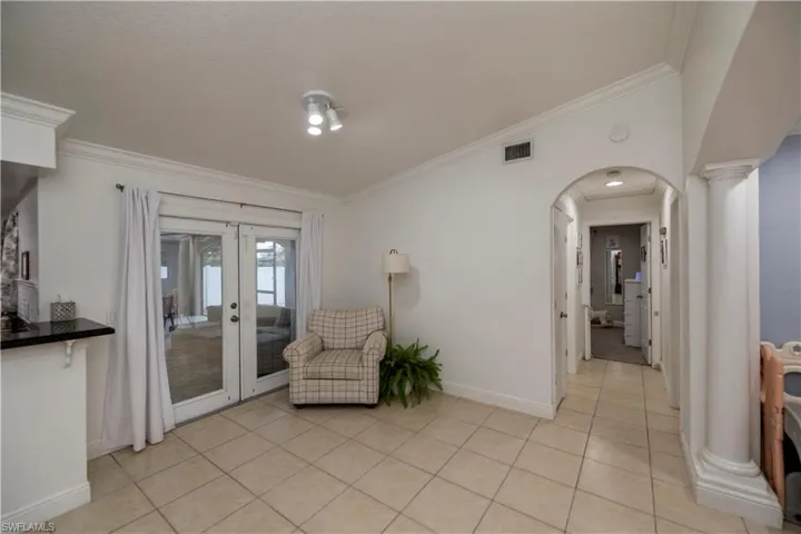 Sitting room featuring light tile floors, ornate columns, ornamental molding, and french doors