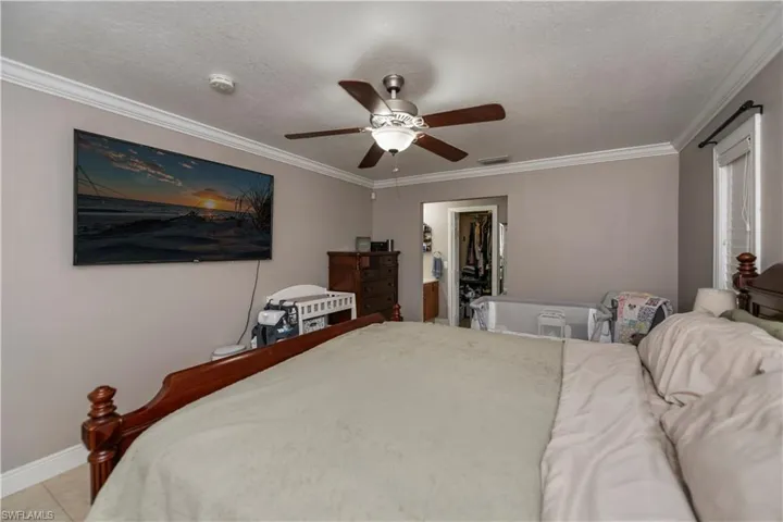 Tiled bedroom with ceiling fan, ornamental molding, a closet, and a walk in closet