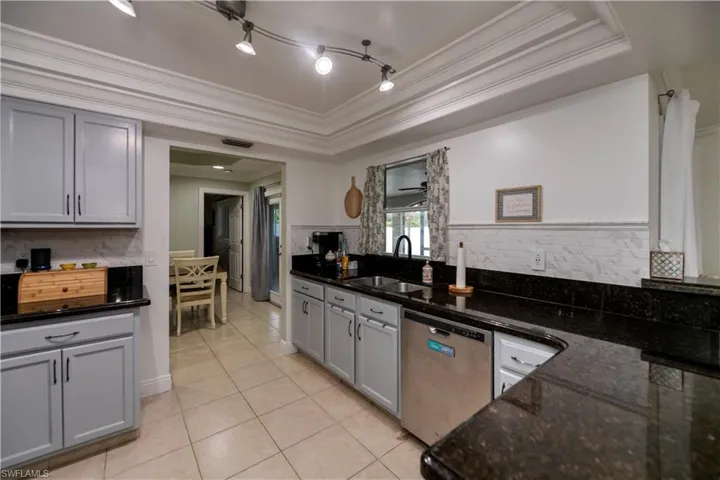 Kitchen featuring a tray ceiling, backsplash, sink, track lighting, and dishwasher