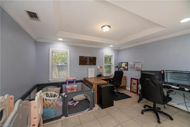 Tiled office space featuring a raised ceiling and crown molding