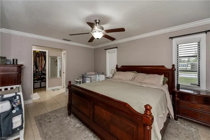 Bedroom with ceiling fan, a closet, crown molding, a spacious closet, and light tile floors