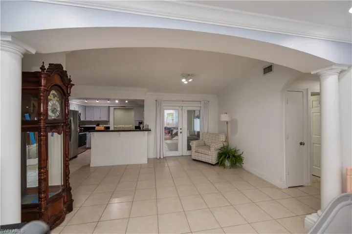 Foyer featuring french doors, decorative columns, ornamental molding, and light tile floors