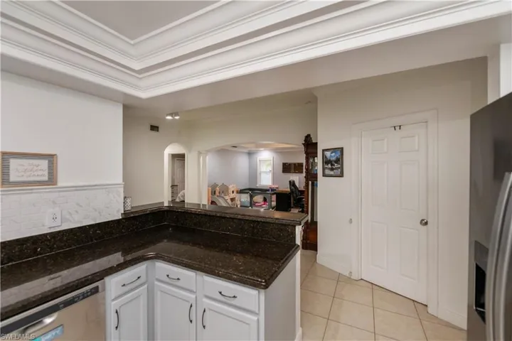 Kitchen with crown molding, dark stone countertops, light tile floors, white cabinets, and appliances with stainless steel finishes