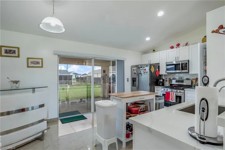 Kitchen with appliances with stainless steel finishes, vaulted ceiling, backsplash, pendant lighting, and light stone counters