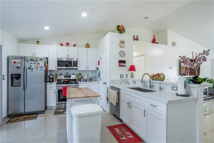 Kitchen featuring appliances with stainless steel finishes, lofted ceiling, butcher block counters, a sink, and a kitchen island