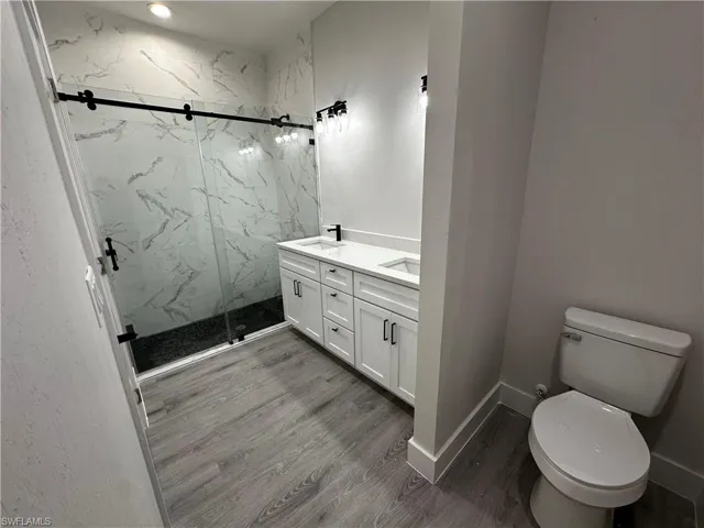 Bathroom with toilet, walk in shower, vanity, and wood-type flooring