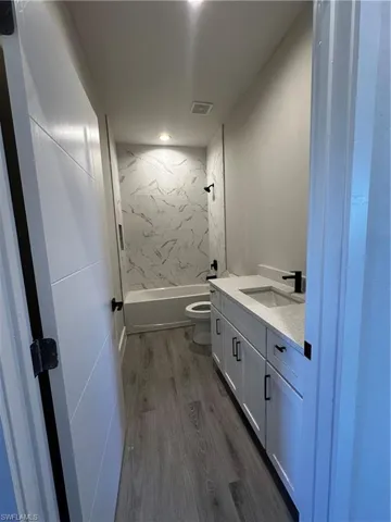 Full bathroom featuring toilet, tiled shower / bath combo, vanity, and wood-type flooring