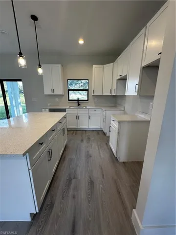 Kitchen featuring a wealth of natural light, dark wood-type flooring, white cabinets, and hanging light fixtures