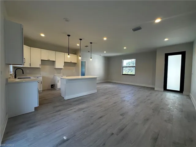 Kitchen with sink, a kitchen island, light hardwood / wood-style floors, pendant lighting, and white cabinets