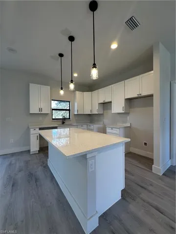 Kitchen with white cabinetry, light stone countertops, dark wood-type flooring, and a kitchen island