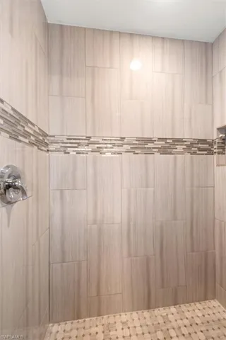 Tiled shower enclosure featuring light-toned large format wall tiles, a decorative mosaic accent band, and a mosaic tile shower floor