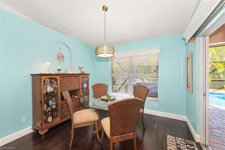 Dining area featuring dark wood-finish flooring, a contemporary pendant light fixture, and a window with blinds