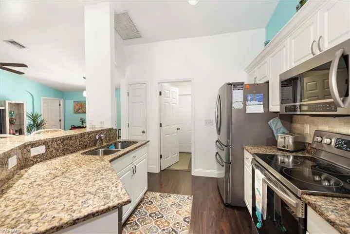 Kitchen featuring stainless steel appliances, granite countertops, white cabinetry, dark wood-finish flooring, and a double basin sink