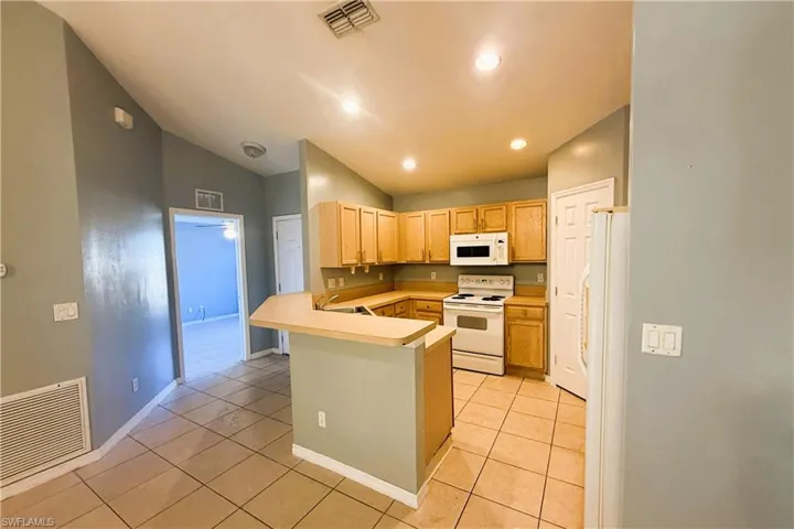 Kitchen featuring white appliances, light countertops, a peninsula, lofted ceiling, and light tile patterned floors