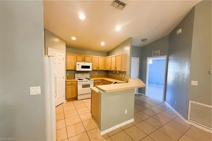 Kitchen featuring white appliances, light countertops, a peninsula, lofted ceiling, and light tile patterned floors