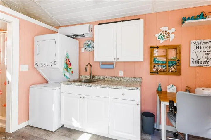 Washroom featuring wooden walls, an AC wall unit, estacked washer and dryer, light wood-style flooring, and cabinet space