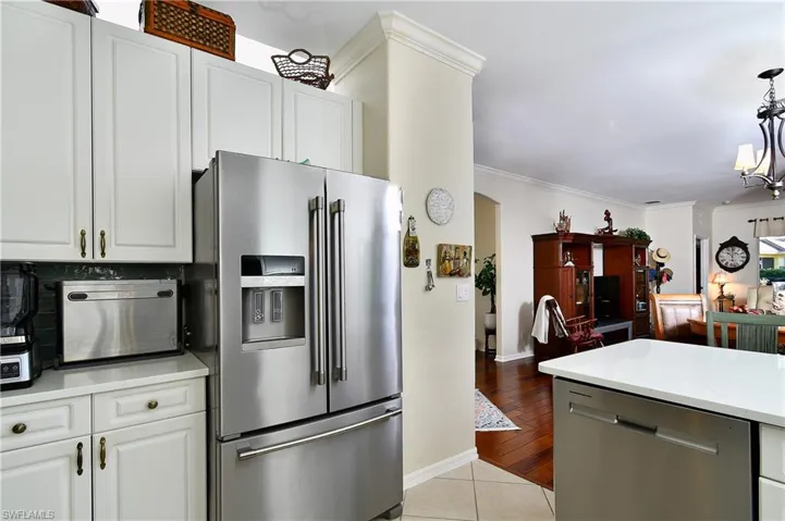 Kitchen featuring ornamental molding, appliances with stainless steel finishes, light stone countertops, and white cabinets