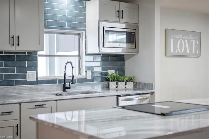 Kitchen with appliances with stainless steel finishes, sink, tasteful backsplash, and light stone counters