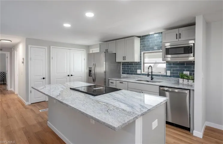 Kitchen with light hardwood / wood-style flooring, backsplash, a center island, sink, and appliances with stainless steel finishes