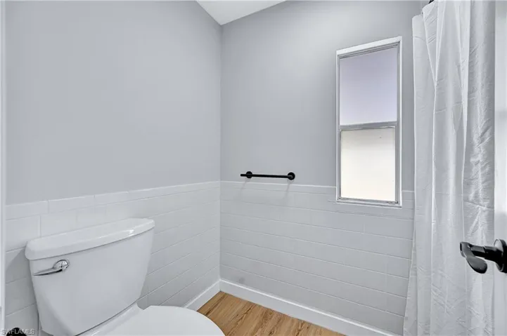 Bathroom with tile walls, wood-type flooring, and toilet