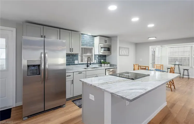 Kitchen with tasteful backsplash, stainless steel appliances, light wood-type flooring, a kitchen island, and sink