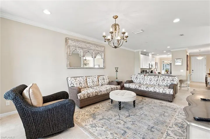 Open-concept interior featuring light-toned tile flooring, recessed ceiling lighting, a wrought-iron style chandelier, and crown molding