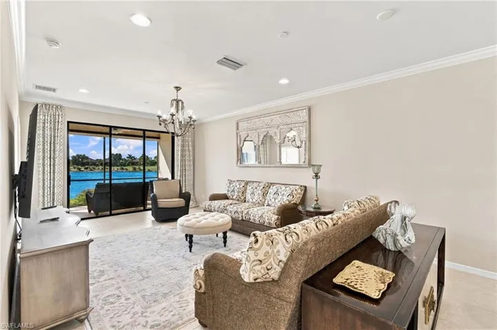 Living area featuring recessed lighting, crown molding, multi-panel sliding glass doors, a decorative wall-mounted mirror, and a multi-arm chandelier