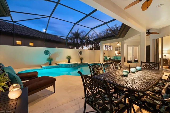 Pool at dusk with ceiling fan, glass enclosure, an outdoor hangout area, and a patio